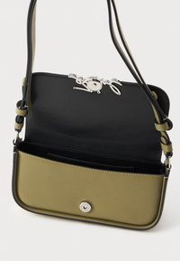 Liten olivgrön axelremsväska med svart inredning, justerbar rem och silverfärgad spänne som är delvis öppen och visar det tomma inredningen.