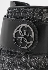 Zwarte laars met een gestructureerde bovenkant met zilveren draden, een gladde zwarte leren band en een glanzend rond logo-accent.