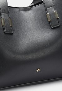 Black leather tote bag with textured surface, featuring two top handles and gold-tone hardware accents. Logo is embossed in gold.