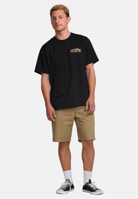 Black cotton t-shirt with a front graphic in colorful lettering, paired with khaki shorts and black sneakers with white laces and socks.