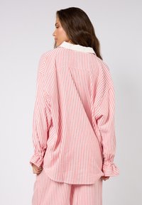 Koszula z długim rękawem w różowo-białe pionowe paski, z klasycznym kołnierzykiem, luźnym krojem oraz elastycznymi mankietami o miękkiej fakturze.