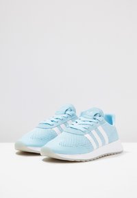 Light blue mesh athletic shoes with white stripes, padded collar, and textured sole. Features lace-up design and breathable upper material.