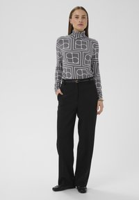 Langærmet grå rullekrave med hvidt geometrisk mønster, kombineret med sorte bukser med vide ben og sorte sko. Armbånd med gulddetalje.