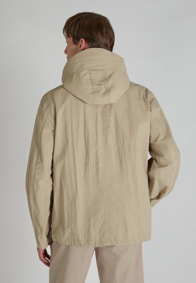 Chaqueta ligera beige con una gran capucha, superficie texturizada y puños elásticos, que presenta un ajuste relajado y detalles de costura en la parte posterior.
