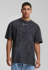 Oversized black acid-wash t-shirt with short sleeves and a round neck, featuring white logo embroidery on the chest. Casual, relaxed fit.