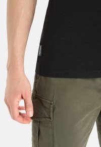 Maglietta nera a maniche corte abbinata a pantaloni cargo verde oliva, con una tasca laterale e un'etichetta in tessuto sulla maglietta.
