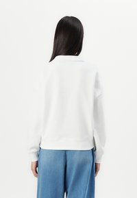 Felpa bianca con colletto alto, polsini e orlo a costine. Texture morbida, vestibilità comoda, abbinata a jeans a palazzo blu chiaro.