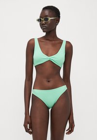 Mintgrön texturerad bikini med en topp med vridning framtill och matchande låg midja nedtill. Har tjocka axelband och design för minimal täckning.