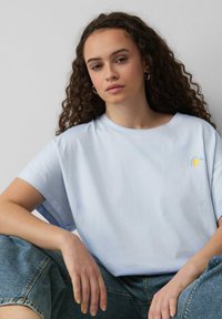 T-shirt en coton bleu clair avec une coupe décontractée, des manches courtes et un petit graphique de citron jaune sur la poitrine gauche. Porté avec un short en denim.