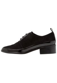 Scarpe in suede nero con trim in vernice lucida e tacco basso a blocco. Caratterizzano un design elegante con punta affusolata e lacci.