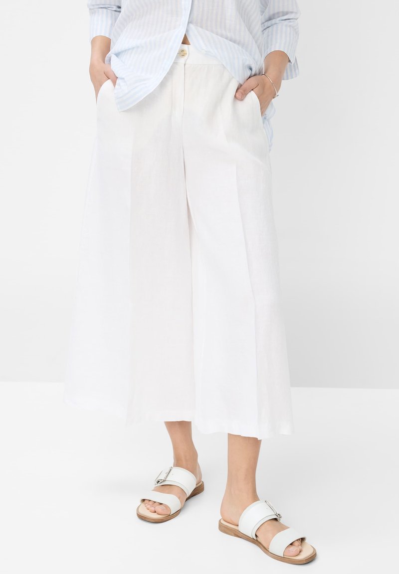 Witte linnen broek met wijde pijpen, plooien en zijzakken, gecombineerd met open-toed witte sandalen met een gesp-accent.