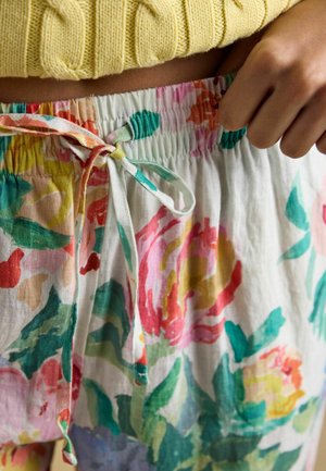 Person adjusting drawstring on elastic waist of floral-patterned light fabric skirt, wearing yellow knitted top.