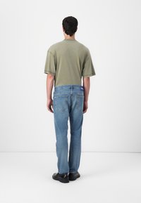 Sivá bavlnená tričko, voľný strih, krátke rukávy; svetlomodré džínsy s vyblednutou textúrou; čierne topánky dopĺňajú neformálny outfit.