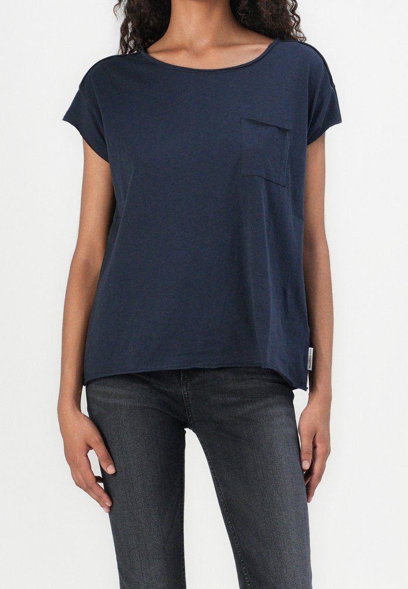 Námořnická modrá krátkosrstá tričko vyrobené z měkkého materiálu, s kapsou na hrudi a volným střihem, spárované s tmavě šedými džíny.