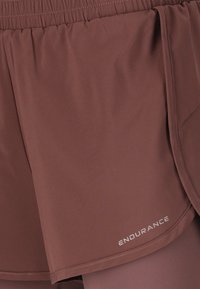 Braune leichte Sportshorts mit elastischem Bund und seitlichen Schlitzen, versehen mit einem reflektierenden "ENDURANCE"-Logo am Saum.
