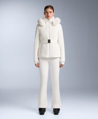 Vit jacka med kabelstickad textur, pälsfodrad huva och svart bälte. Kombinerad med smala vita byxor och platåskor, mot en neutral bakgrund.