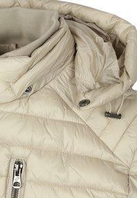 Beige pufferjack met een geribde kraag, gedetailleerde stiksels, ritsluiting en metalen accenten. Lichtgewicht en een gladde textuur.