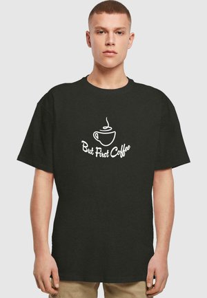 Schwarzes Baumwoll-T-Shirt mit kurzen Ärmeln, das ein weißes Grafikdesign einer Kaffeetasse sowie den Text "Aber zuerst Kaffee" in einer lässigen Schriftart zeigt.