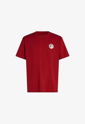 Camiseta roja de algodón con cuello redondo y mangas cortas, con un logo circular en el área del pecho izquierdo. Textura suave en toda la prenda.