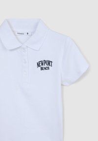 Polo bianco realizzato in tessuto a coste, con maniche corte e colletto. Testo ricamato che recita "NEWPORT BEACH" in nero.