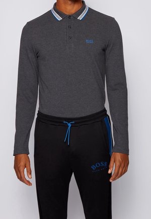 Homme portant un polo à manches longues gris foncé avec col rayé bleu et un pantalon de jogging noir avec cordon bleu et logo "BOSS".