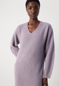 Gaiši lavandas krāsas adīta kleita ar V-veida kakla izgriezumu, garām piedurknēm un ribotu tekstūru. Mīksta, ērta auduma ar smalku apdari gar kakla izgriezumu.