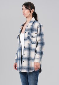 Blauw en crèmekleurig geruit overhemd van zachte stof, met knoopsluiting aan de voorkant, borstzak en lange mouwen. Gestyled met denim jeans.
