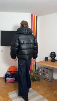 Svart puffjacka med glansig yta, oversized huva och distinkt quiltad design. Kombinerad med vida mörka denimjeans.