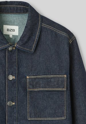 Veste en denim bleu foncé avec un col, fermeture à boutons et une poche à patch. Présente des coutures contrastées et un tissu texturé.