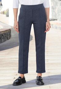 Marineblauwe broeken met een visgraatpatroon, een op maat gemaakte pasvorm, een voorplooi en opgerolde manchetten. Gecombineerd met zwarte instapschoenen.