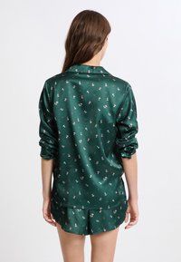 Grünes Satin-Schlafanzugset mit einem kurzärmeligen Hemd mit Kragen und Knopfleiste, verziert mit einem kleinen Blumenmuster, ergänzt durch Shorts.