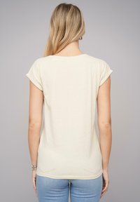 Helebeige T-särk rullitud varrukatega, millel on pehme ja sile tekstuur ning ümar alläär. Tagapoolt vaadatuna on disain lihtne.