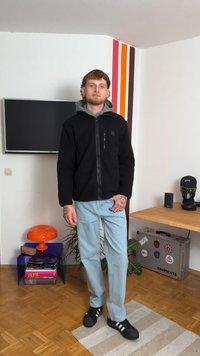 Musta tõmblukkudega kapuutsiga jakk halli sisepinnaga, heledad sinised teksad ja mustad spordijalatsid. Tätoveeringud on nähtavad kätele. Siseõhk.