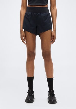 Zwarte sportshorts met een brede tailleband en een gesplitst ontwerp. Gecombineerd met zwarte kniekousen en hardloopschoenen.