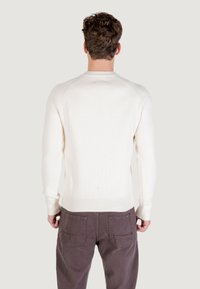 Pullover di maglia a coste color crema con scollo rotondo e maniche raglan. Indossato con pantaloni marrone scuro. La superficie appare morbida e lavorata a maglia.