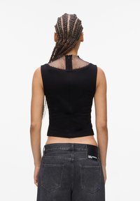 Black sleeveless crop top with a textured netted back and a small zipper. Paired with dark grey high-waisted jeans featuring a label.