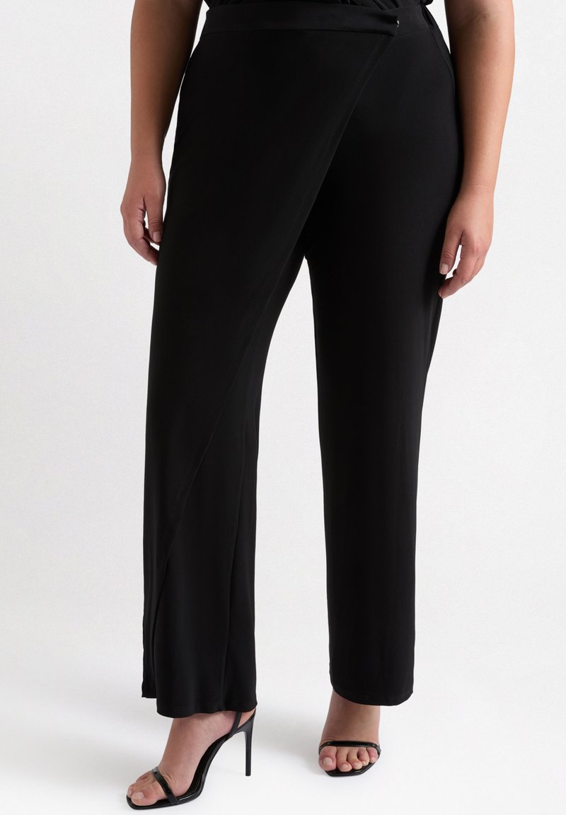 Zwarte wijde broek gemaakt van gladde stof, met een asymmetrisch ontwerp aan de voorkant en een strakke zoom. Gecombineerd met zwarte hoge hakken sandalen.