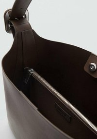 Brown leather handbag interior, featuring a zippered pocket with silver hardware and a smooth texture. Strap attachment visible.