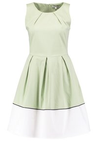 Robe verte sans manches à plis, avec une jupe blanche et un ourlet bordé de noir. Tissu lisse avec un corsage ajusté.