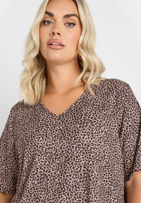 V-ringad leopardmönstrad topp i mjukt, ljusrosa tyg med svarta fläckar; lös passform och korta ärmar, lämplig för avslappnad användning.