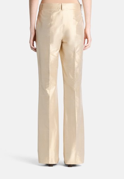 Back view of person wearing high-waist, wide-leg beige satin trousers, standing against a plain light background.