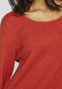 Roter Strickpullover mit rundem Ausschnitt und weicher Textur. Der Stoff wirkt leicht und hat eine etwas lockere Passform an den Schultern.