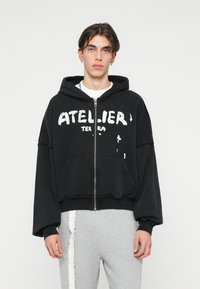 Sweatshirt capuz preto feito de algodão, apresentando um fecho frontal, grande texto gráfico branco e um corte relaxado com bolsos canguru.