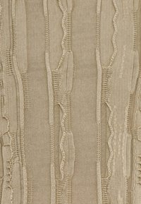 Beige tekstil med strukturerede mønstre af bølgede og lineære designs, med varierende tykkelser og et blødt strikket udseende.