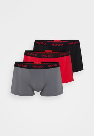 Drie paar Hugo heren boxershorts in grijs, rood en zwart. Elk heeft een zwarte tailleband met een herhalend "Hugo" logo.