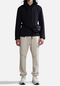 Rompevientos azul marino con puños elásticos y capucha, combinado con pantalones de chándal ajustados de color claro que presentan detalles de costura y zapatillas blancas.