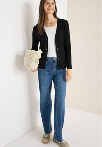 Czarny prążkowany kardigan na pięć guzików, noszony na białym topie. Połączony z jasnoniebieskimi jeansami o prostych nogawkach i beżowymi tenisówkami.