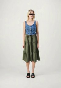 Denim top with buttons and green tiered skirt. Model wears black open-toe shoes and sunglasses. Simple, two-tone design.