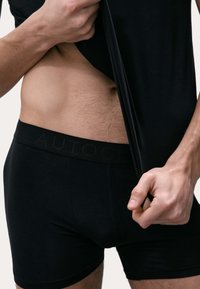 Černé boxerky s texturovaným pasem s logem "AUTOGRAM", těsně přiléhající, vyrobené z měkké elastické tkaniny. Nad nimi je viditelná kůže.