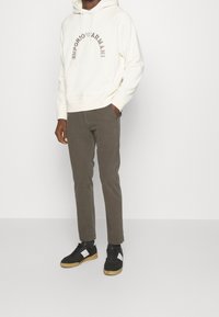 Vit hoodie med "Emporio Armani" logotyp, olivgröna byxor och svarta sneakers med vita och krämfärgade detaljer. Slät tygtextur.